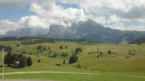 Backwards aerial of perfect green hills on a sunny day with large mountains in the background, Val Gardena, Alpe di Siussi, Dolomites photo