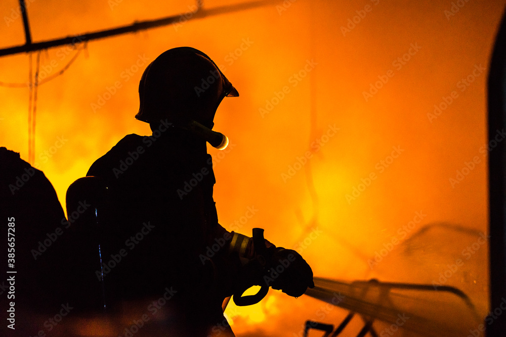 Silhouettes of strong and brave firefighter using water and extinguisher to fighting with fire flame in an emergency situation.