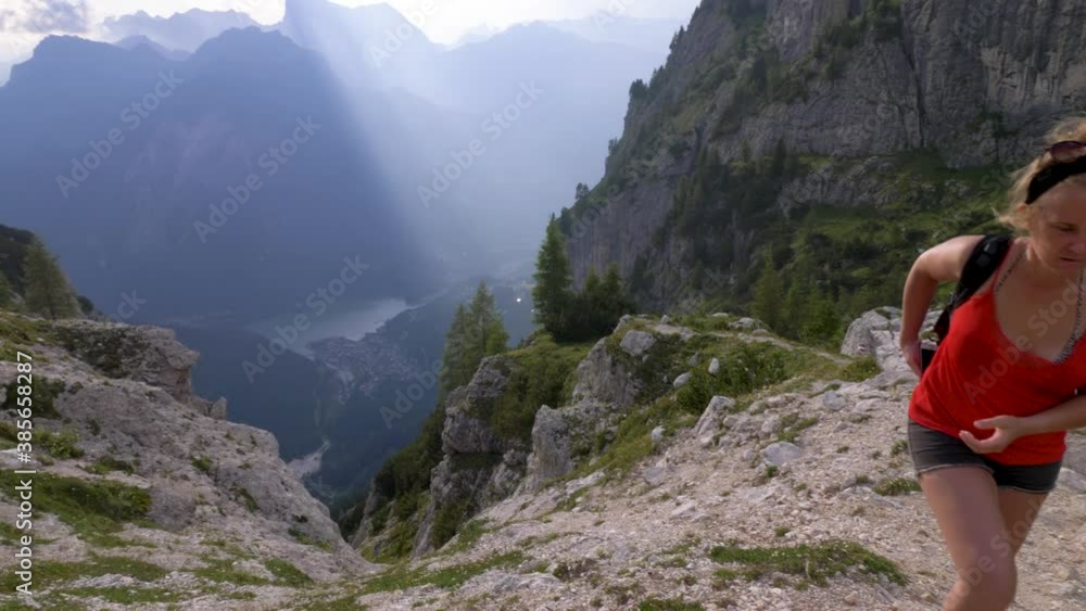 Blonde female tourist in a red shit, putting her phone away and continuing the hike in a beautiful mountain range in Europe Blonde female tourist in a red shit, putting her phone away and continuing the hike in a beautiful mountain range in Europe