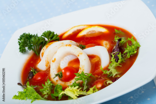 Beautifully served bowl with tomato soup with squid and greens