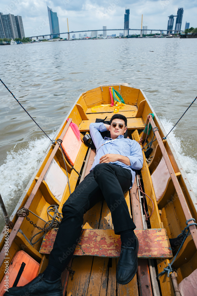 Business man wear sunglasses sleep on wooden boat in Bangkok.