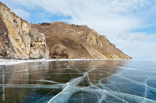 Baikal Lake on sunny frosty day in February. Beautiful smooth transparent ice near the rocks of the famous Sagan-Zaba Сape with ancient rock paintings. Ice travel. Natural background. Winter landscape photo