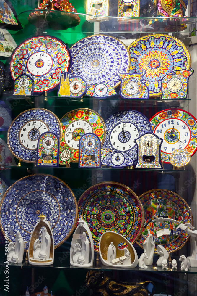 Colorful mosaic ceramic plates, mugs, clocks on showcase of Barcelona gift shop. Traditional souvenirs