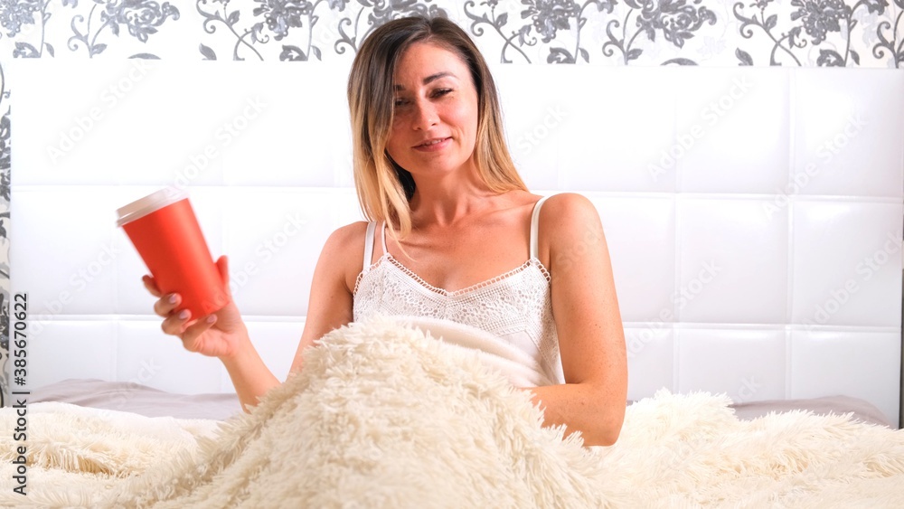 funny woman rises in bed with takeaway coffee, enjoys the morning and drinks coffee. The concept of starting a new day, relaxing on the weekend, no need to rush anywhere, good morning funny woman rises in bed with takeaway coffee, enjoys the morning and drinks coffee. The concept of starting a new day, relaxing on the weekend, no need to rush anywhere, good morning