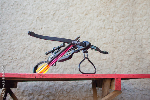 Fotografija A black crossbow with a telescopic sight lies on a table in the yard