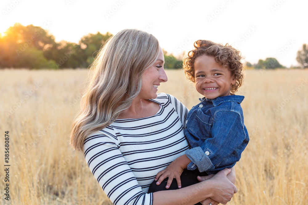 Beautiful happy Mother holding her adorable diverse son in the outdoor sunlight. Sun rays shining through as the mom shows love and affection to her son Beautiful happy Mother holding her adorable diverse son in the outdoor sunlight. Sun rays shining through as the mom shows love and affection to her son