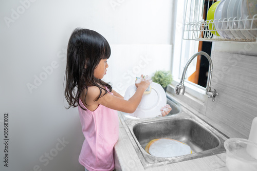 asian little girl wash the dishes in the kitchen