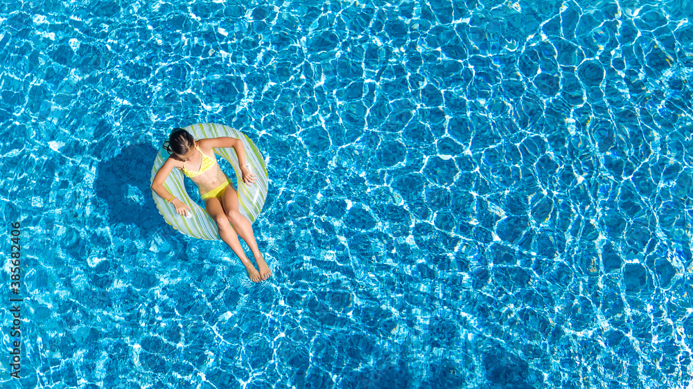 Aerial drone view of little girl in swimming pool from above, kid swims on inflatable ring donut , child has fun in blue water on family vacation resort
