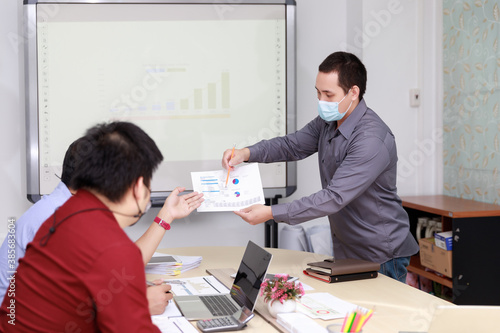 Businessmen wearing protective masks discussing and work together in meeting room. Social distance practice prevent coronavirus COVID-19.