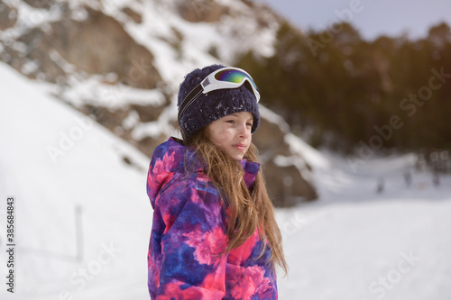 beautiful adorable active little american girl in ski suit wool hat and goggles on outdoor snow winter mountain resort background