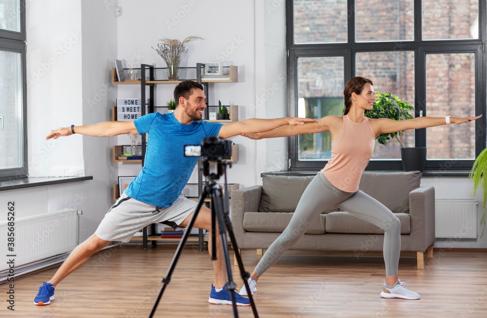 fitness, sport and video blogging concept - couple of bloggers with camera on tripod recording online yoga class at home fitness, sport and video blogging concept - couple of bloggers with camera on tripod recording online yoga class at home