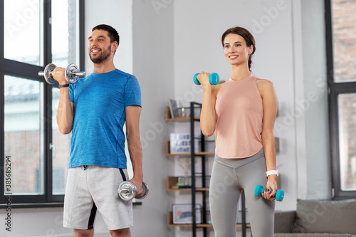 sport, fitness, lifestyle and people concept - smiling man and woman exercising with dumbbells at home