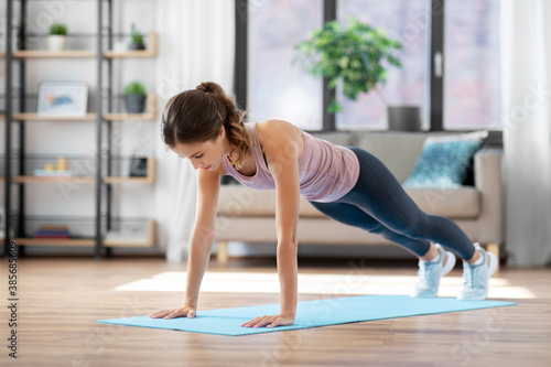 fitness, sport, training and people concept - young woman doing high plank exercise on mat at home