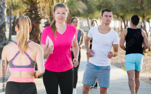 Sporty women and men running along embankment in sunny morning