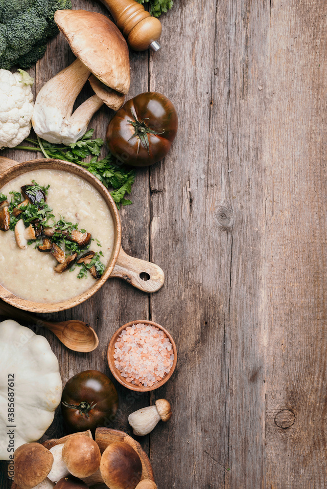 Homemade vegetarian mushroom soup with fried mushrooms, vegetables, spices, raw boletus edulis mushroom on wooden background. Top view. Copy space. Autumn harvest concept