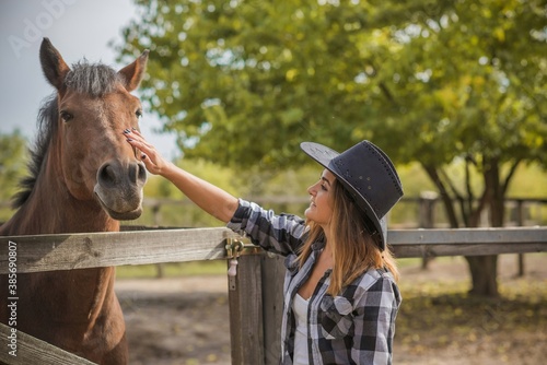 American woman on a horse farm. Portrait of girl in cowboy hat with a horses. Hippotherapy at nature