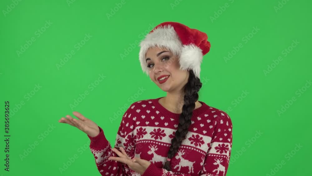 Portrait of sweety girl in Santa Claus hat is talking and pointing side hand for something, copy space.. Green screen Portrait of sweety girl in Santa Claus hat is talking and pointing side hand for something, copy space.. Green screen
