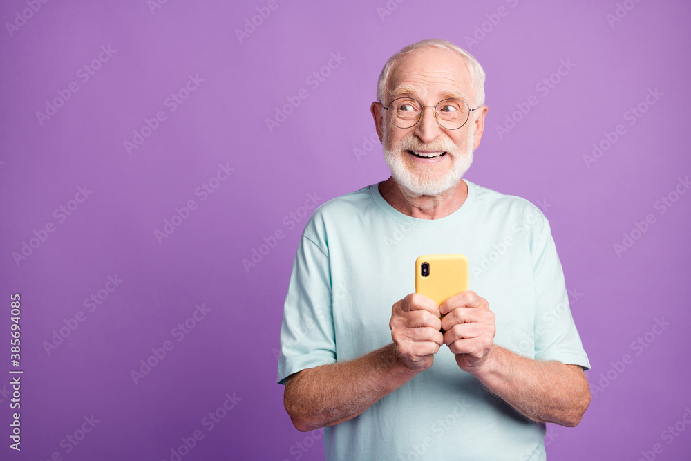 Photo portrait of elderly man holding phone in two hands looking at blank space isolated on vivid purple colored background Photo portrait of elderly man holding phone in two hands looking at blank space isolated on vivid purple colored background