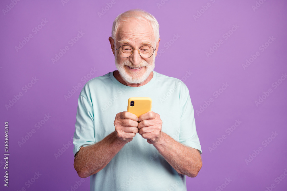 Photo portrait of engaged elderly man holding phone in two hands isolated on vivid purple colored background Photo portrait of engaged elderly man holding phone in two hands isolated on vivid purple colored background