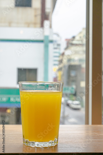 A glass of fresh orange juice drink on brown table with downtown window view background.