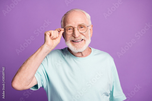 Portrait of positive grey hair beard grandfather touch eyeglasses wear blue t-shirt isolated on purple color background