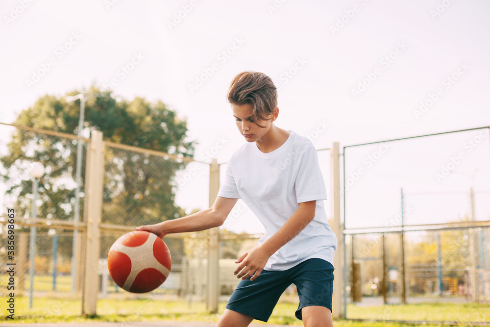 Focused cute boy athlete leads the ball in a game of basketball. A boy plays basketball after school. Sports, healthy lifestyle, leisure Focused cute boy athlete leads the ball in a game of basketball. A boy plays basketball after school. Sports, healthy lifestyle, leisure