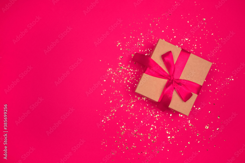 Gift box with red bow on festive bright pink background with golden sparkles around and copyspace for your text. Flat lay style. Christmas, New Year, Valentines Day or birthday celebration concept