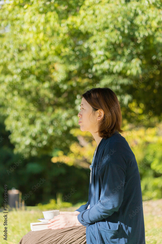 Naklejka premium 秋の公園でコーヒーを飲みながら読書している女性の姿