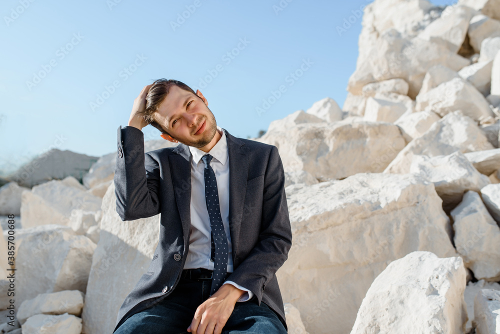 man in classic clothes, jacket, tie and glasses is sitting on the chair and posing on the mountain. man in classic clothes, jacket, tie and glasses is sitting on the chair and posing on the mountain.