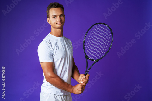 Caucasian young man tennis player posing with tennis racket against purple background © fotofabrika