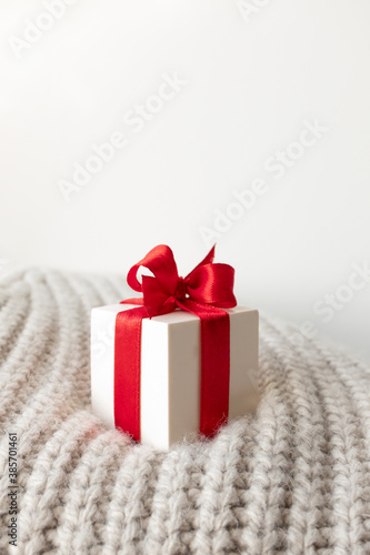 Close-up white gift box with red ribbon bow on beige warm knitted sweater © Olha Kozachenko