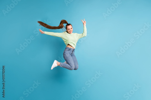 Full length body size side profile photo of jumping girl with long hair showing v-sign isolated on vibrant blue color background