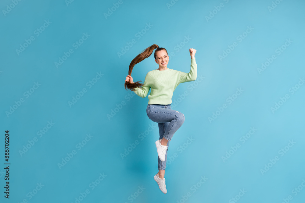 Full length body size photo of jumping high girl long ponytail gesturing like winner isolated on bright blue color background Full length body size photo of jumping high girl long ponytail gesturing like winner isolated on bright blue color background