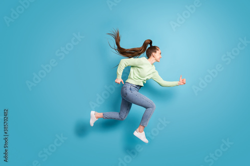 Fototapeta Naklejka Na Ścianę i Meble -  Full length body size side profile photo of jumping high running fast girl with long hair ponytail isolated on bright blue color background