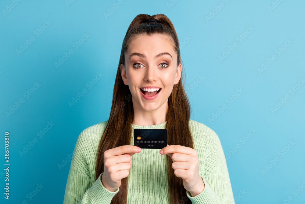 Photo portrait of excited girl holding bank card with two hands open mouth isolated on pastel blue colored background Photo portrait of excited girl holding bank card with two hands open mouth isolated on pastel blue colored background