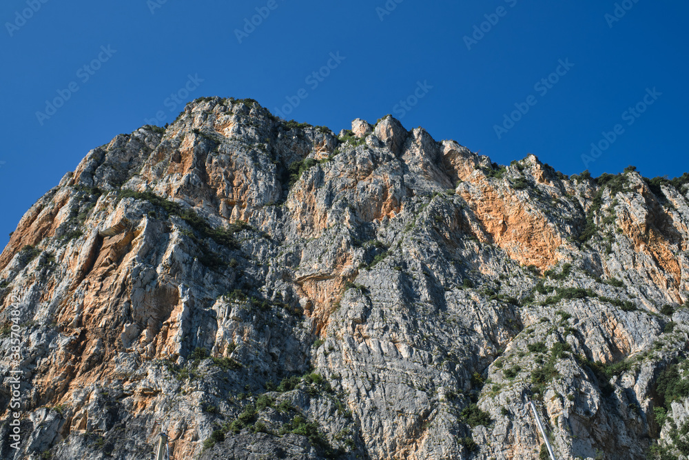 Gray rocks at high altitude. Alps top on blue sky. Rough rocky stones. Red stones on a blue background. The tops of the yellow peaks of the rocks.