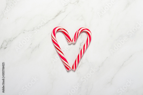Caramel cane folded in the shape of a heart on a marble background. Concept Christmas, New Year, sweets for the holiday. Flat lay, top view
