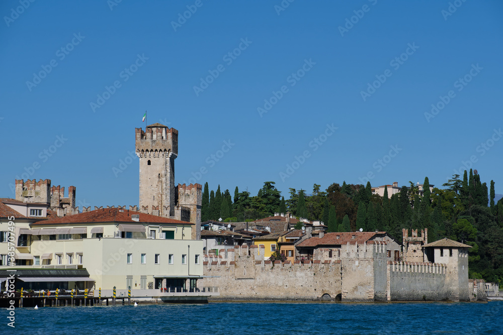 Town of Sirmione entrance walls view, Lago di Garda, Lombardy region of Italy. Autumn in Italy on Lake Garda, Sirmione peninsula. Trees in the autumn season. Town of Sirmione entrance walls view, Lago di Garda, Lombardy region of Italy. Autumn in Italy on Lake Garda, Sirmione peninsula. Trees in the autumn season.