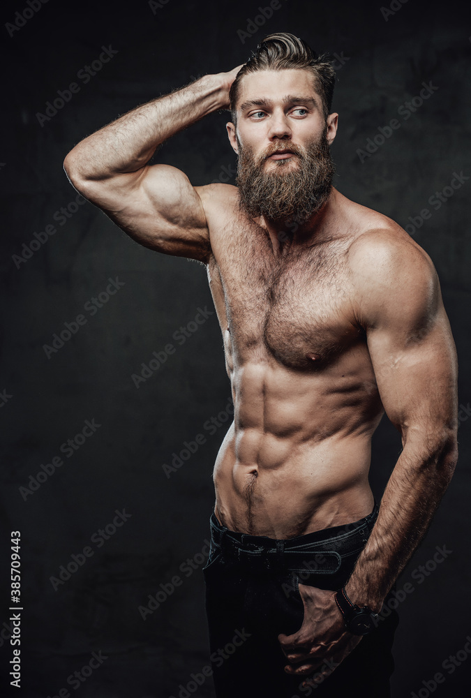 Fototapeta premium Cool and haired shirtless man with beard and moustache in pants posing with hand in pockets and hand under head in studio.