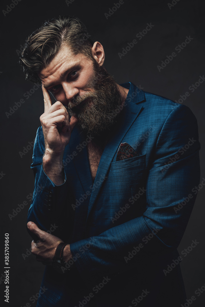 Brutal and handsome man with beard and stylish haircut posing with finger to his head in dark background. Brutal and handsome man with beard and stylish haircut posing with finger to his head in dark background.