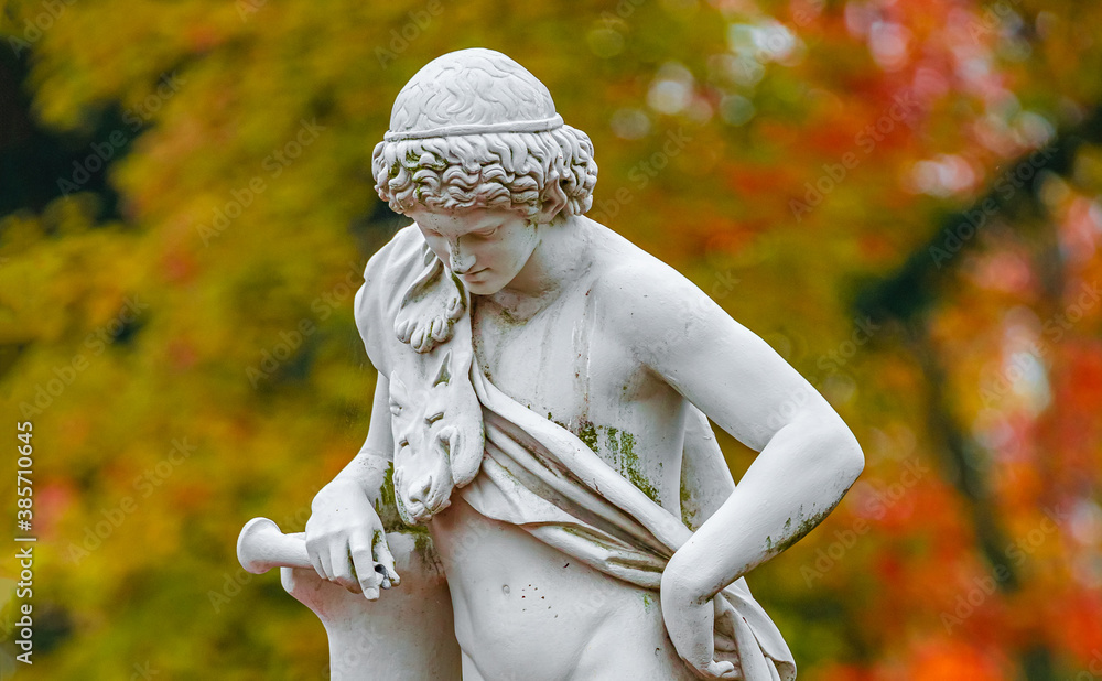 Old park statue of Renaissance Era Roman man hunter in lion skin with hunting tube in golden Autumn city park, Potsdam, Germany Old park statue of Renaissance Era Roman man hunter in lion skin with hunting tube in golden Autumn city park, Potsdam, Germany