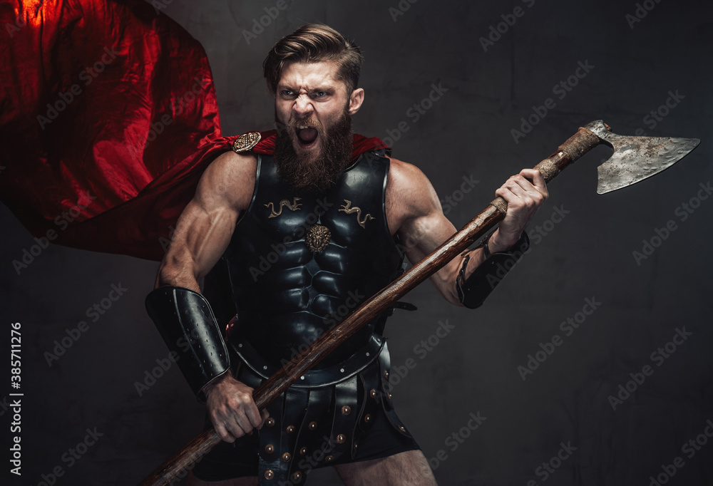 Naklejka premium Aggressive combat rome warrior with beard in black armor screaming holding his two handed axe in dark background.
