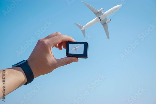 male hand with camera filming an airplane in the sky