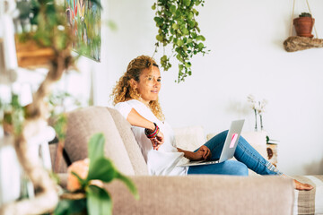 Beautiful woman work and have relax at home with laptop computer - concept of smart work and alternative office - female enjoy technology on the couch and smile - modern lady with connection
