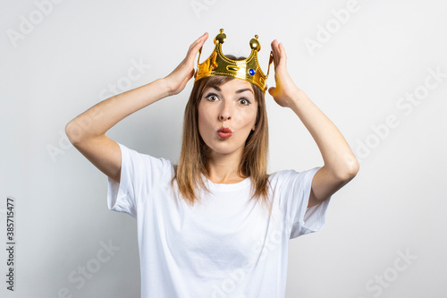 Young woman with a crown on her head with a surprised face on a light background. Emotion laughter, surprise, shock. Concept of a queen, luck, wealth, gain, victory, dream, goal, aspiration. Banner