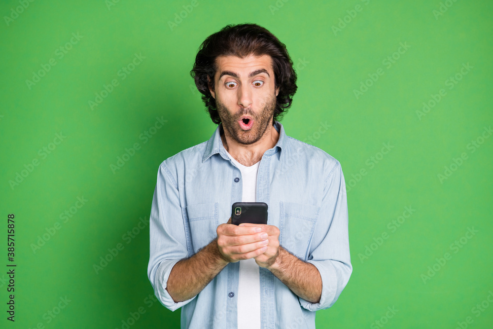 Photo of man hold telephone shocked expression open mouth staring screen wear jeans shirt isolated green color background Photo of man hold telephone shocked expression open mouth staring screen wear jeans shirt isolated green color background