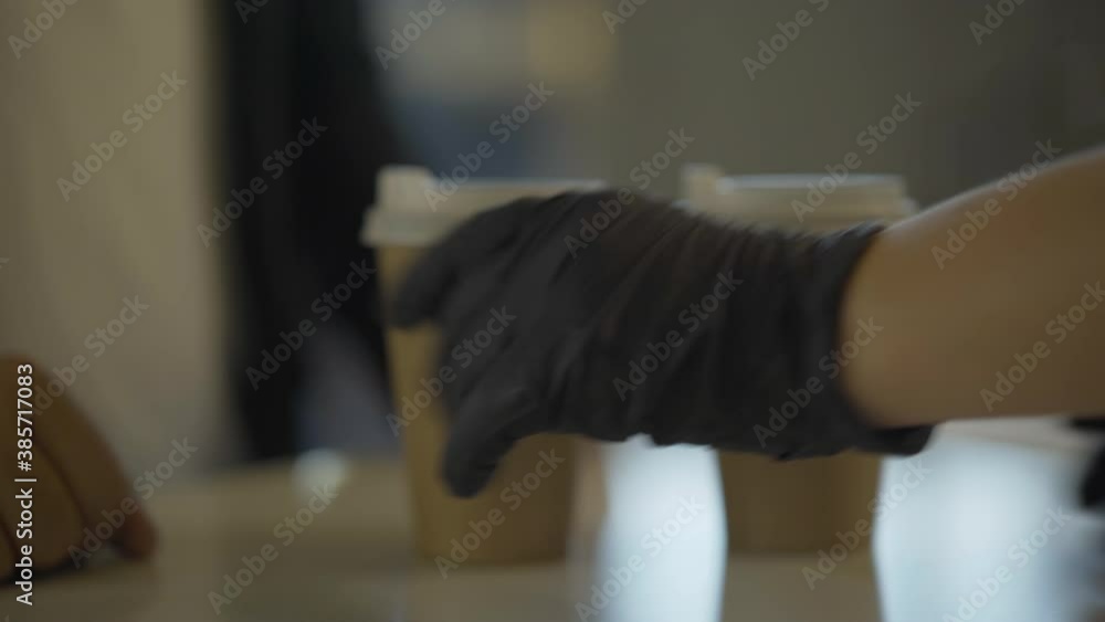 Side view of barista hands passing takeaway coffee to client. Unrecognizable Caucasian woman in protective gloves serving hot drink for man. Coronavirus restaurant business. Side view of barista hands passing takeaway coffee to client. Unrecognizable Caucasian woman in protective gloves serving hot drink for man. Coronavirus restaurant business.