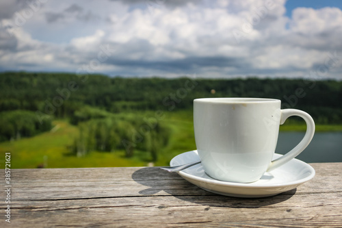 White cup of hot coffee on balcony with natural and mountains, hills background. Copy space.