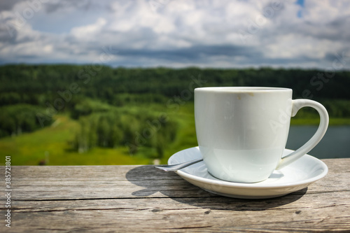 White cup of hot coffee on balcony with natural and mountains, hills background. Copy space.