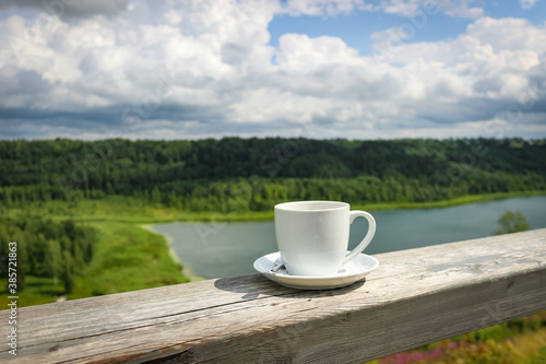 White cup of hot coffee on balcony with natural and mountains, hills background. Copy space.